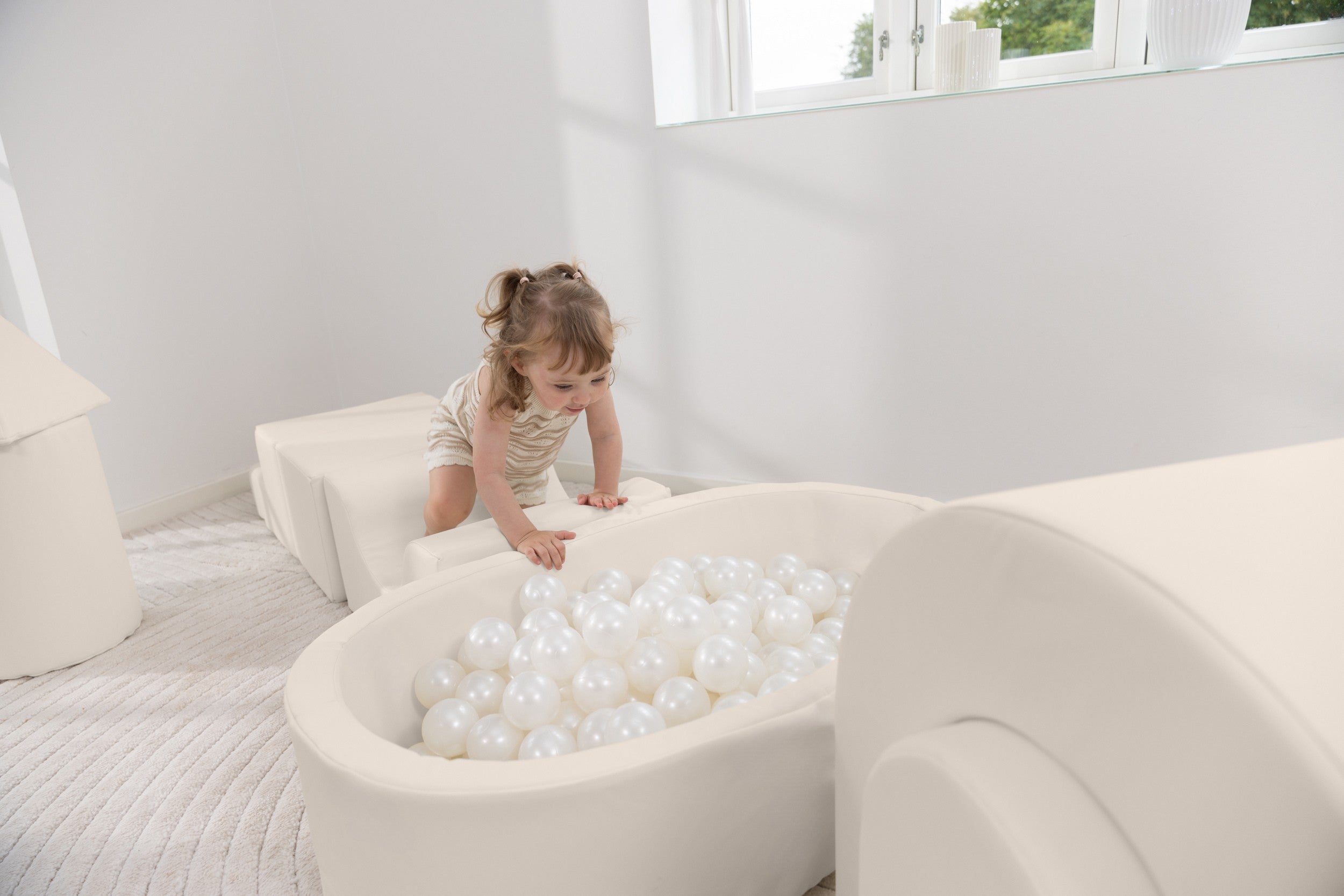Child playing with white balls in a ball pit inside a modern living room.